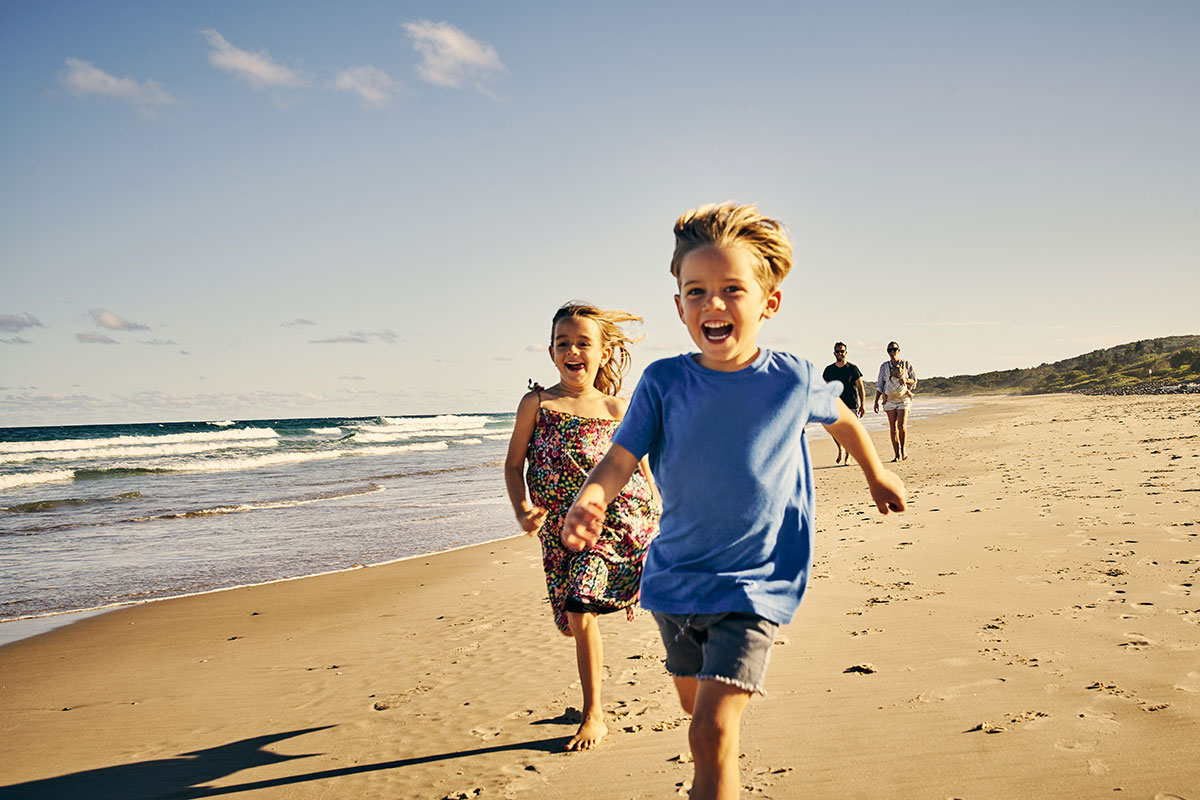 Two younger kids running on the beach with their parents walking behind | Motif
