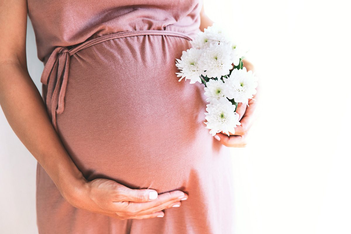 A mother in a dress holding flowers next to her baby bump | Motif