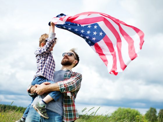 A father holding his son who is holding an American Flag | Motif
