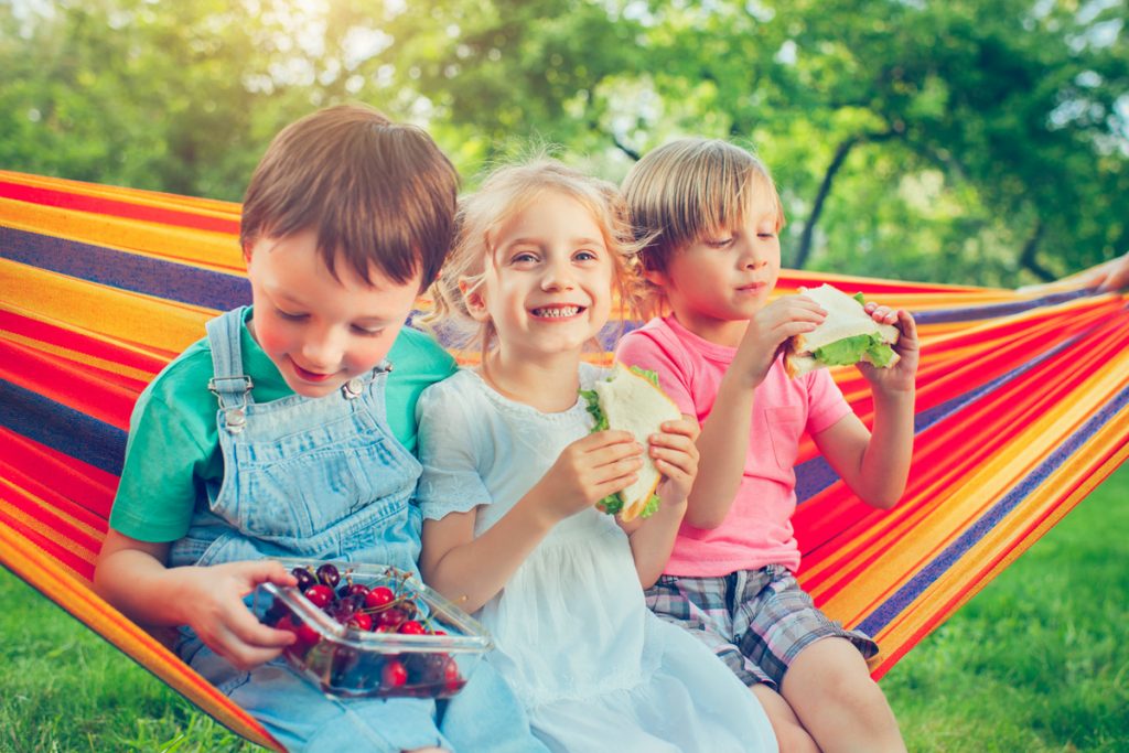 Photography of kids sitting on a hammock and eating snacks | Motif