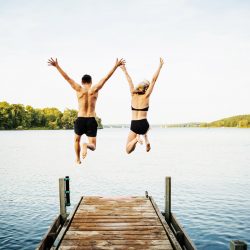 Two friends jump off a pier into the lake