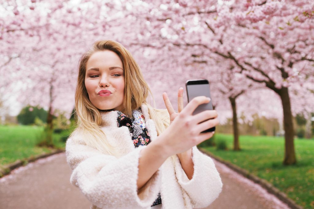 Cute young woman at spring blossom park taking self portrait