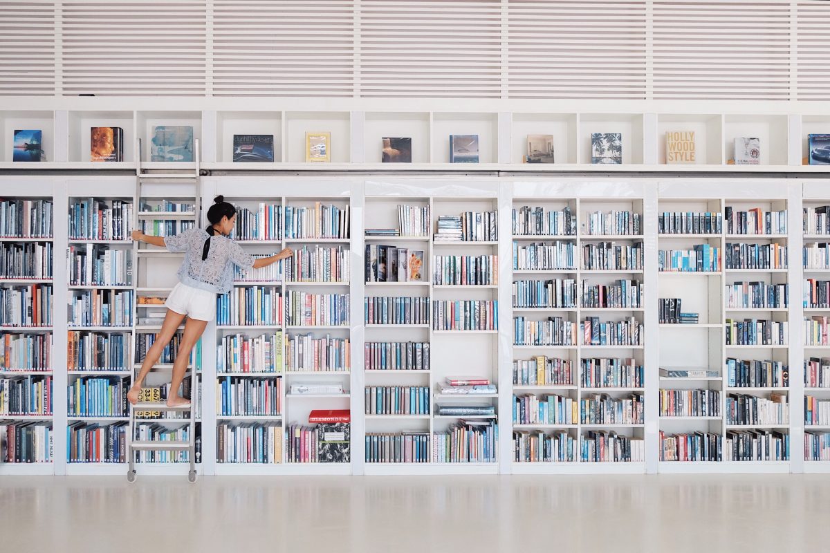 A young woman organizing a large bookshelf.