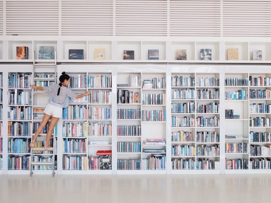 A young woman organizing a large bookshelf.