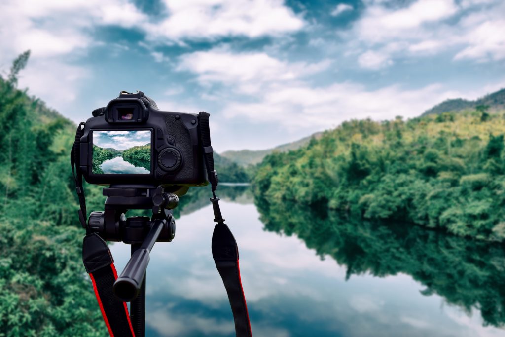 Nature photographers use a tripod to capture a steady shot of mountains and a river.