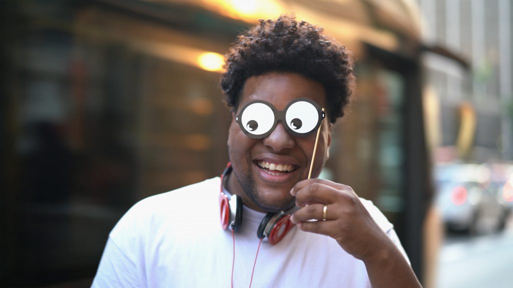 Young man in white shirt holds googly-eye prop to his face for a funny selfie idea.