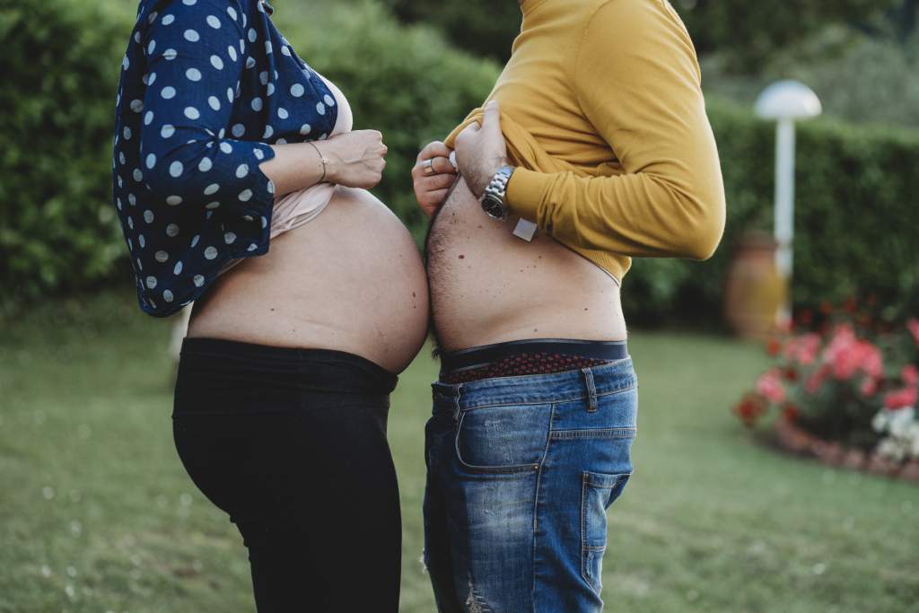 Pregnant woman touches bare belly to husband’s bare belly to make a funny picture idea.