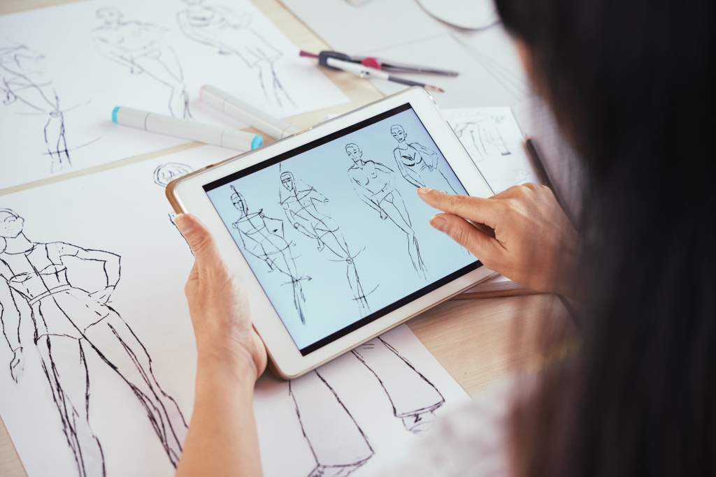 Woman looks at fashion sketches on a tablet to use for a photo book idea.