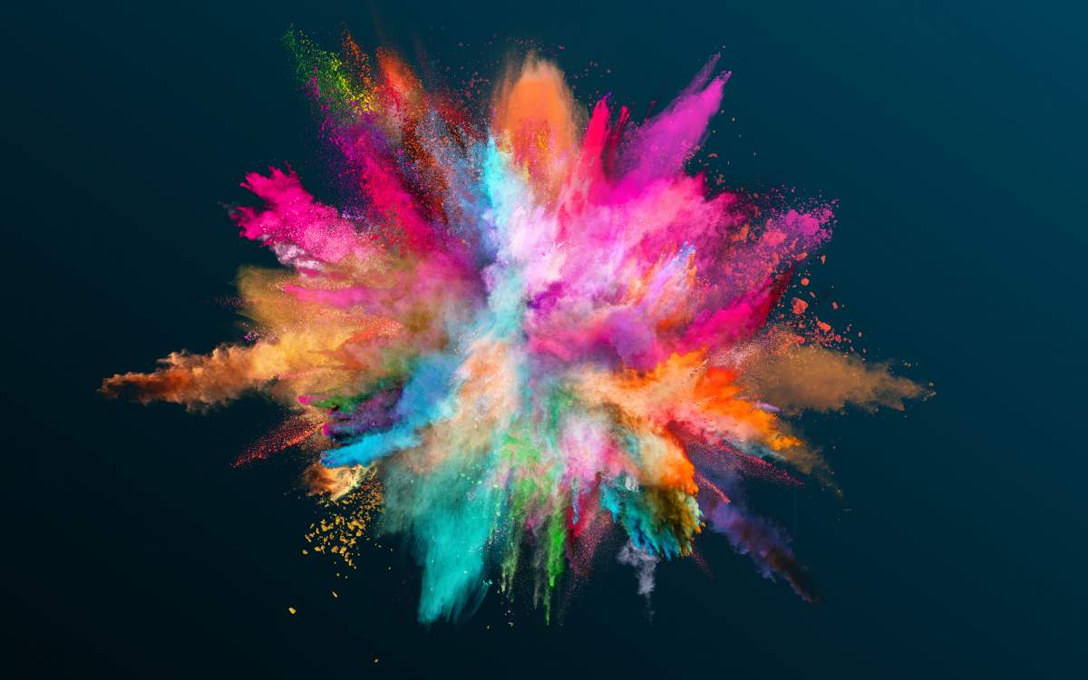 Various color powder explodes on black background to inspire better photo book design.