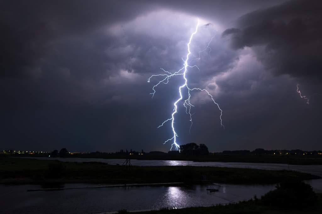 Lightning bolt striking river landscape is captured using these night photography tips.