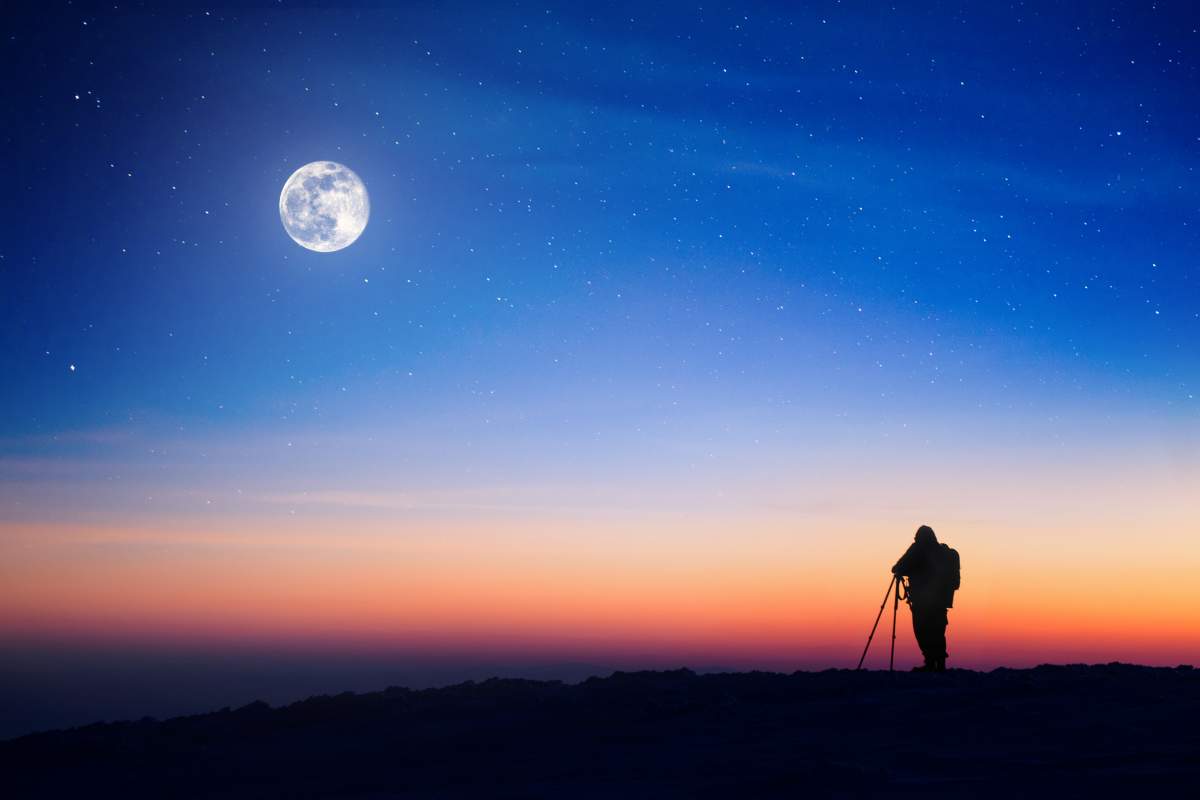 Photographer with tripod uses night photography tips to shoot the moon at sunset.