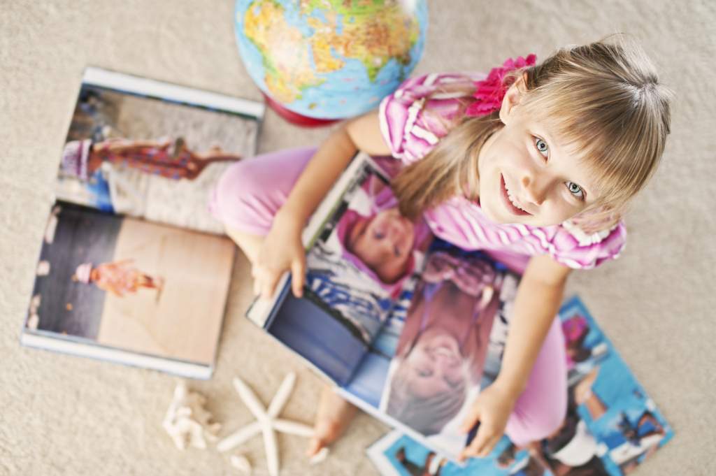 Little girl in pink looks through family vacation photo books for ideas.  