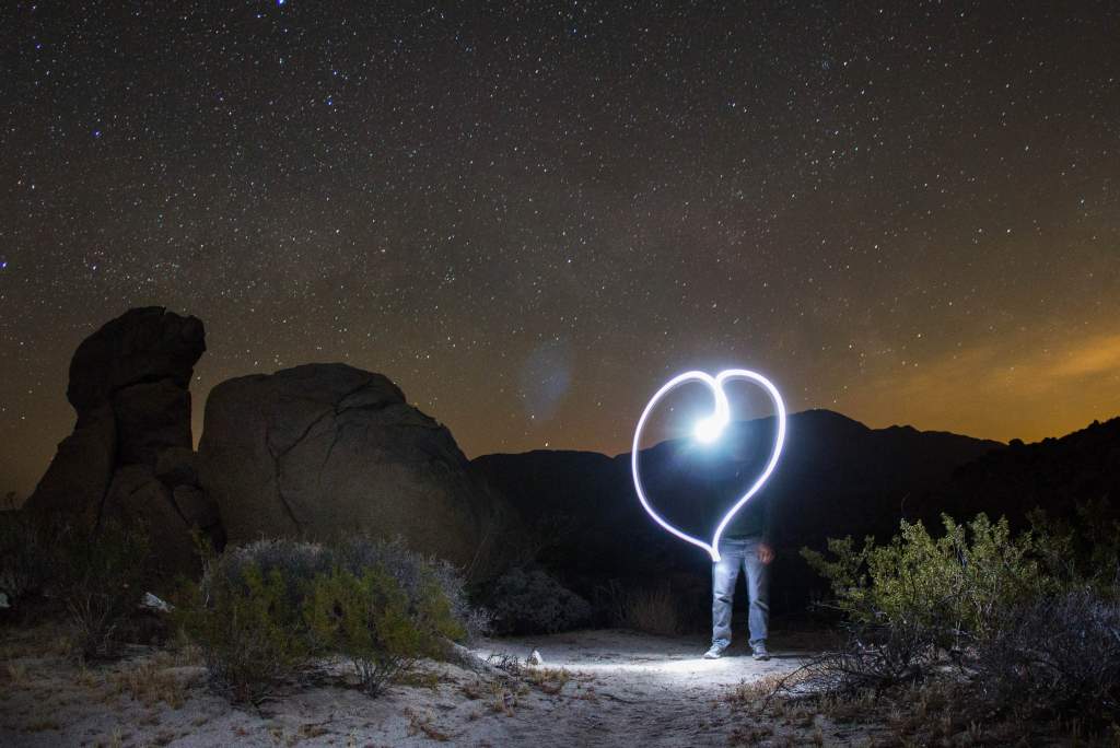 Night photography tips create light-painted heart in front of a man’s face in the desert.
