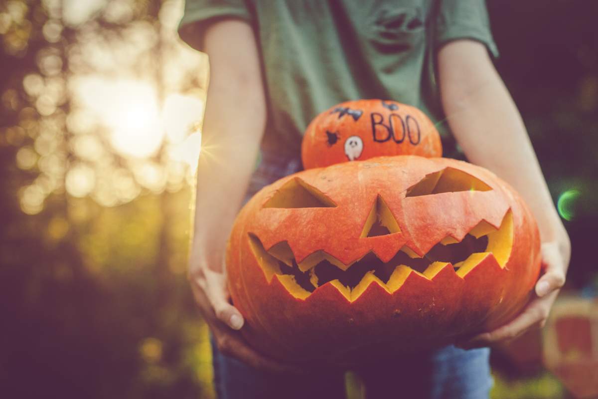 Woman’s hands holding a small gourd and a carved pumpkin to take cute Halloween photos.