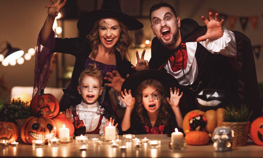 Mom, dad & two kids pose for cute Halloween photos with candles, pumpkins & scary faces.