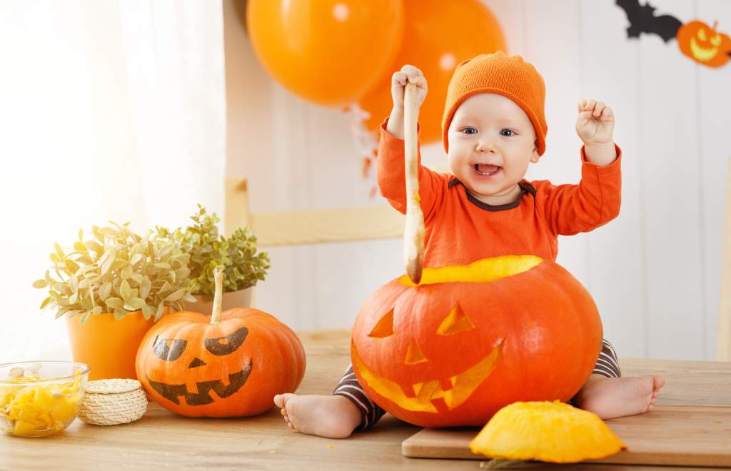 A baby sitting with jack-o-lantern on kitchen counter makes for cute Halloween photos.