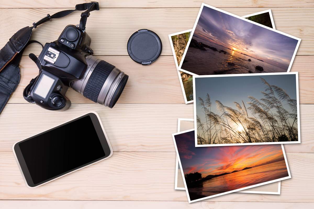 A smartphone, a camera and printed photos on wood background illustrate iPhone vs. DSLR debate.