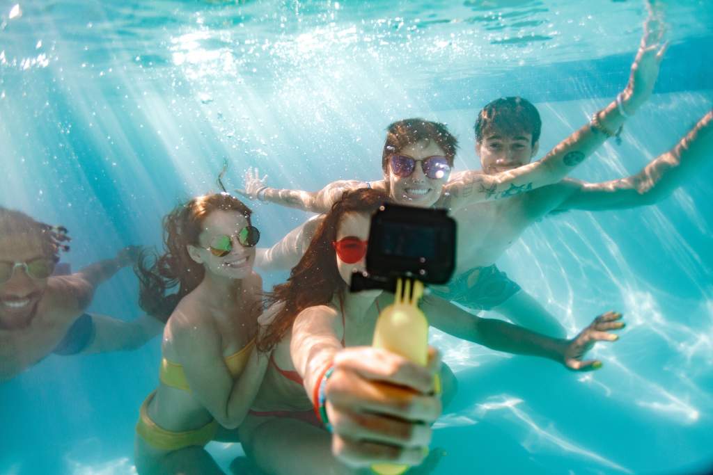 Five young men and women take a selfie with GoPro underwater in a pool.