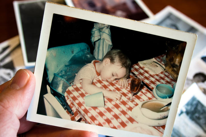 Hand holds vintage photo of a little boy at the table in Thanksgiving food-coma nap.