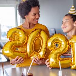 Mom & young son wear festive hats and hold ‘2021’ balloons at home to take New Year’s Eve pictures.