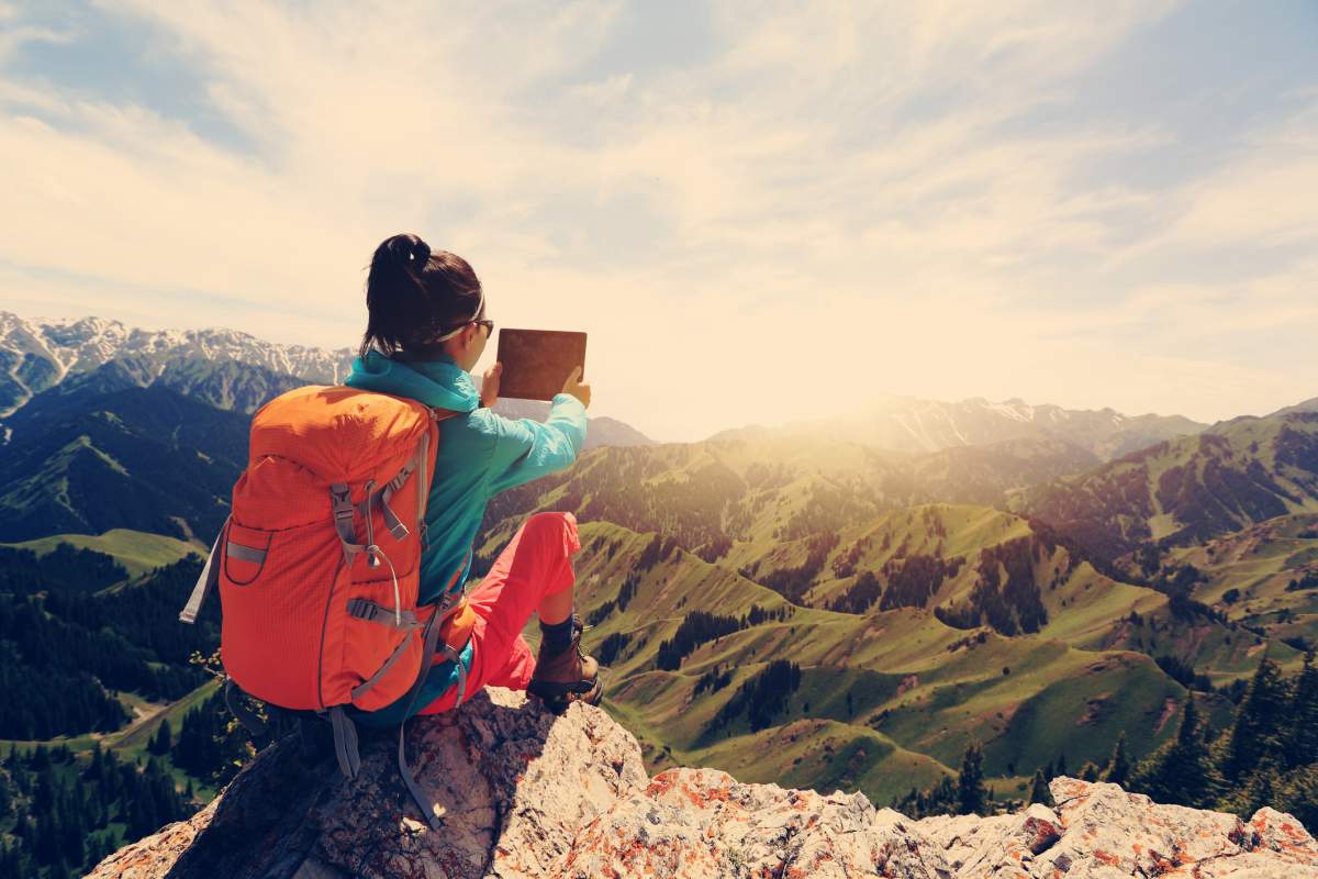 woman backpacker use digital tablet taking photo on mountain peak