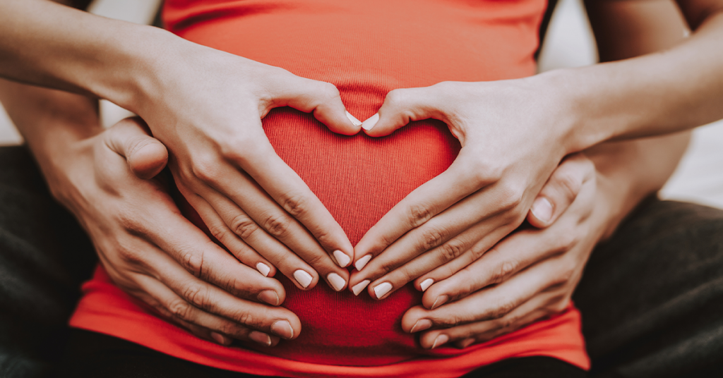 A heart sign on a pregnant belly is a classic maternity photo shoot pose.