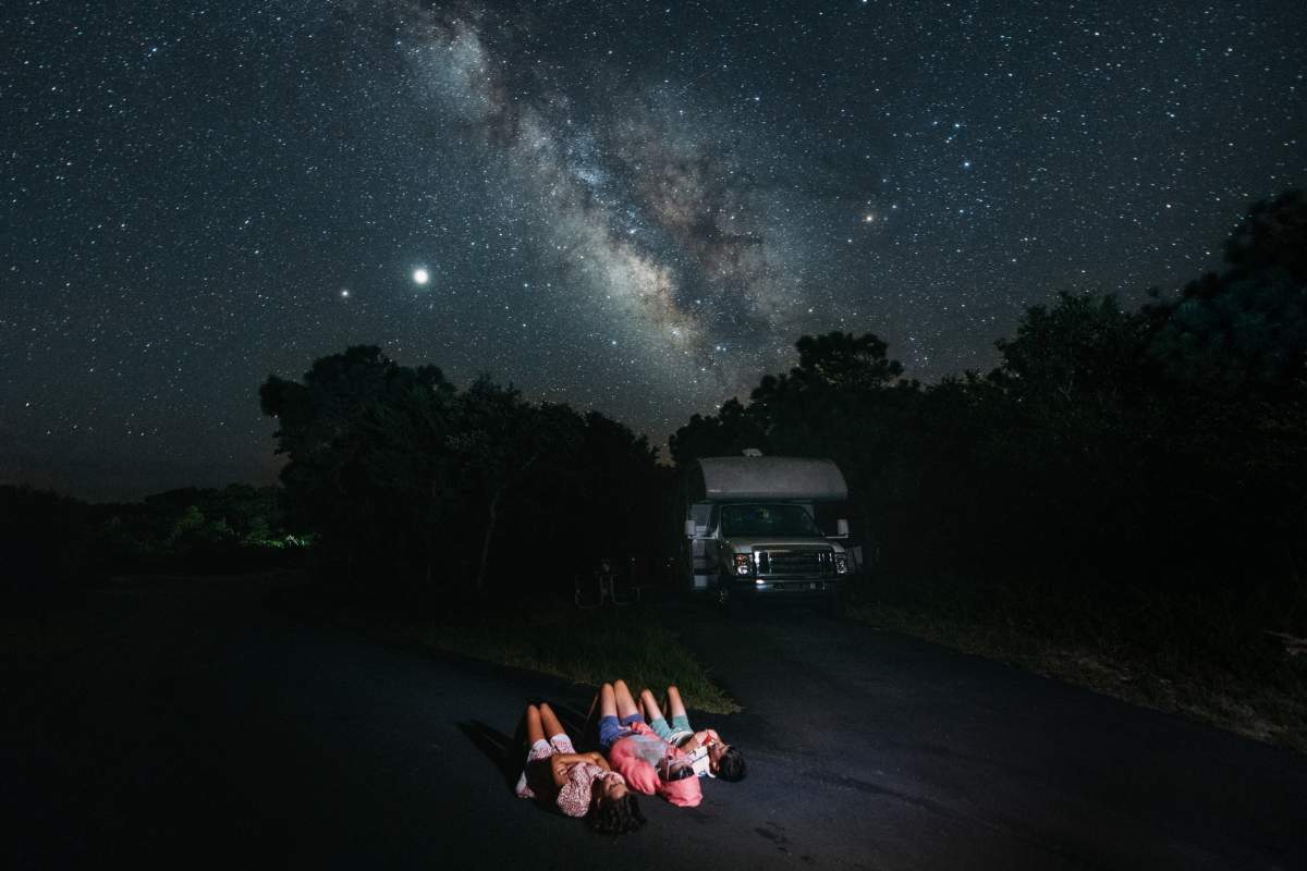 Family lies on the ground by RV looking at the stars