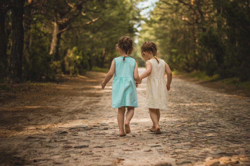 Photo of two cute twins walking along a forest road