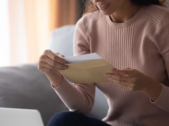 Smiling young woman holding envelope with paper letter.